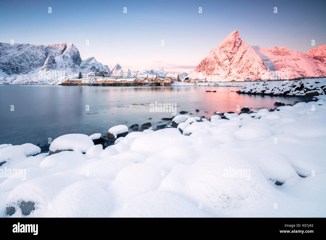 I colori dell'alba telai le case di pescatori circondato da vette innevate Sakrisøy Reine Nordland Isole Lofoten in Norvegia Europa Foto Stock