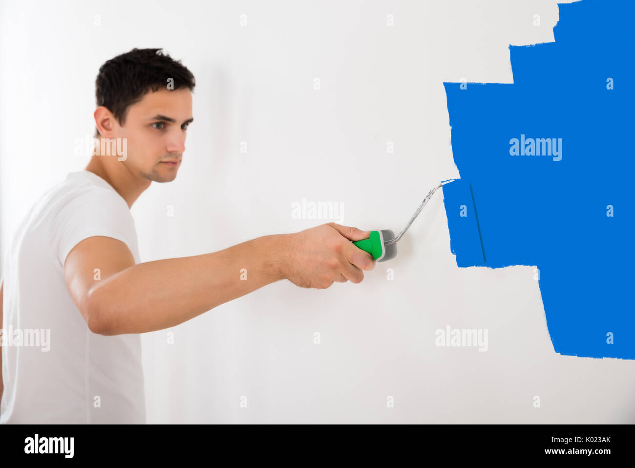 Giovane uomo parete di verniciatura con vernice blu il rullo a casa Foto Stock