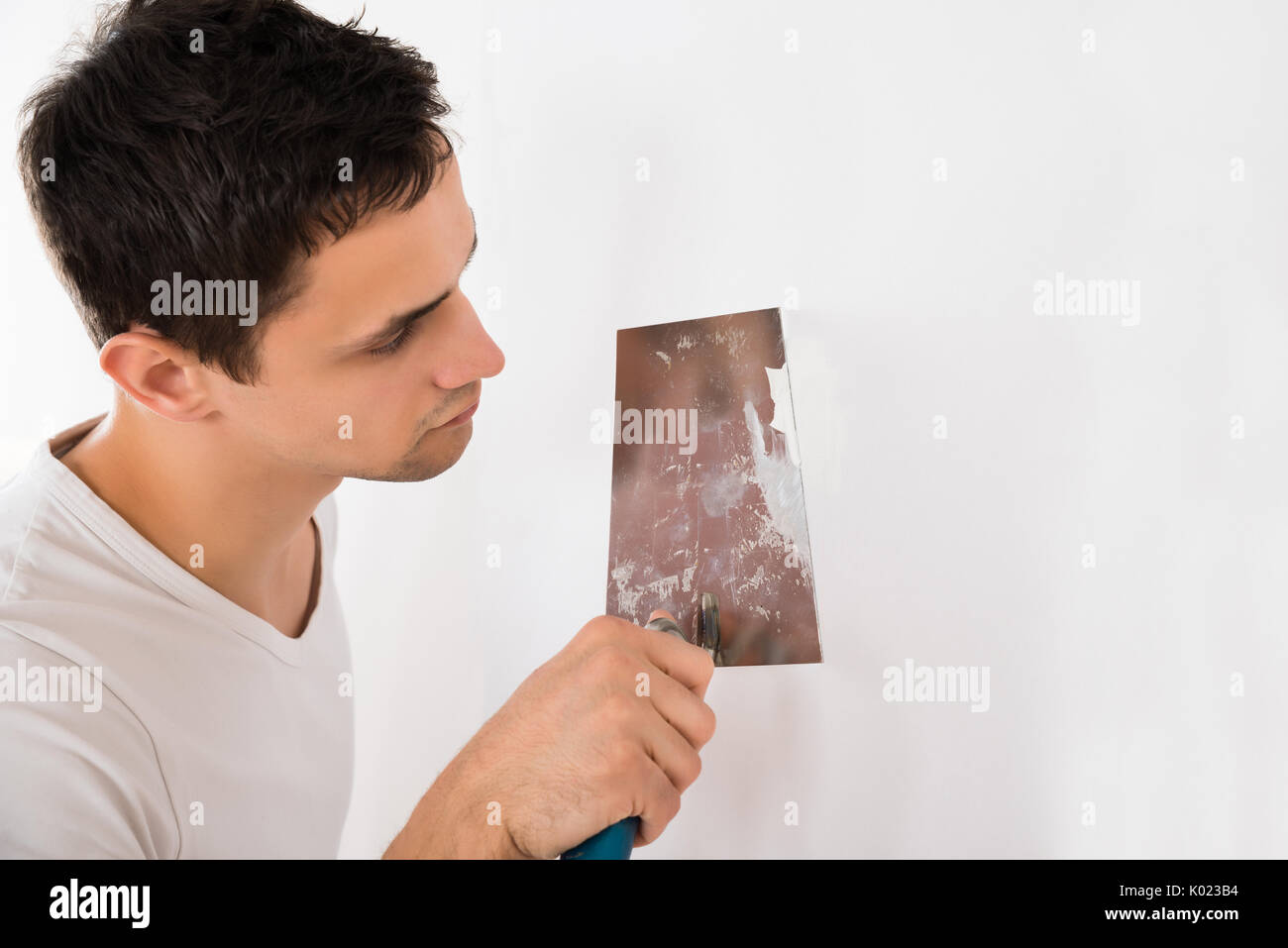 Giovane uomo mediante spatola sul muro bianco a casa Foto Stock