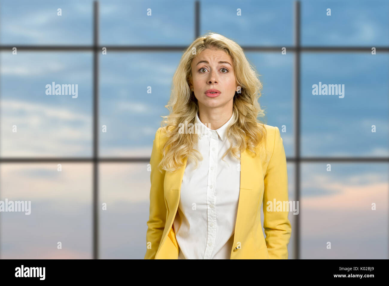 Ritratto di deluso giovane donna. Bella bionda ricalcato cercando confuso su blue sky office lo sfondo della finestra. Le espressioni facciali umane. Foto Stock