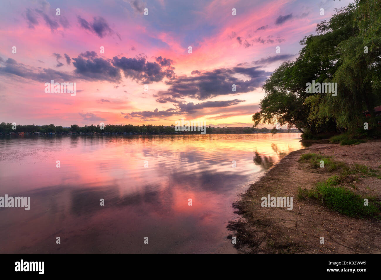Tranquillo paesaggio con fiume e colorato il cielo con le nuvole al tramonto. Un paesaggio fantastico con il lago, spiaggia, red sky con multicolore nuvole riflettono in wa Foto Stock