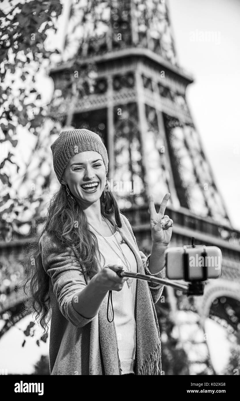 Fughe d'autunno a Parigi. sorridente giovane donna elegante sul terrapieno vicino alla Torre Eiffel a Parigi, Francia tenendo selfie con cellulare e mostra victor Foto Stock