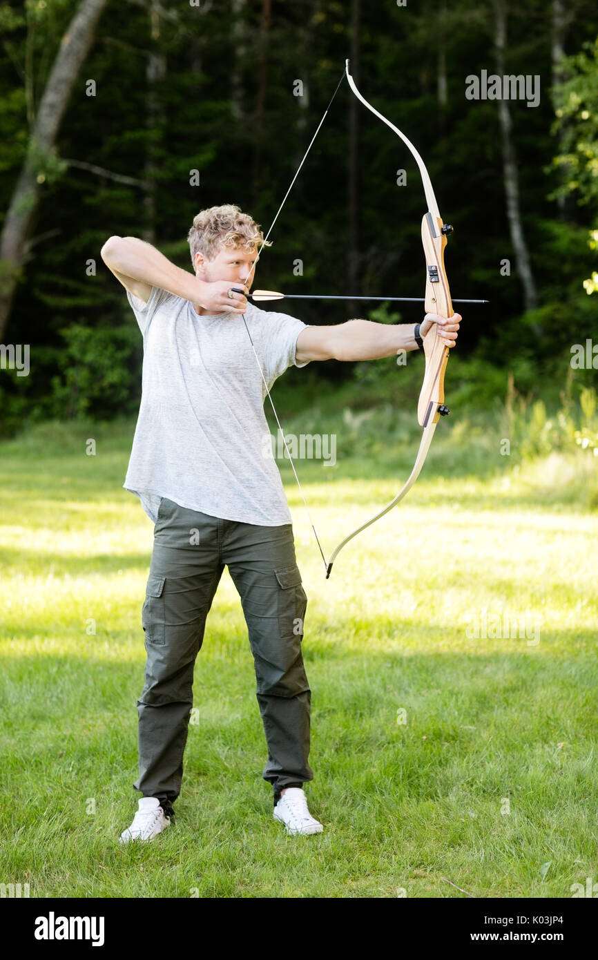 Uomo fiducioso puntando con arco e frecce nella foresta Foto Stock