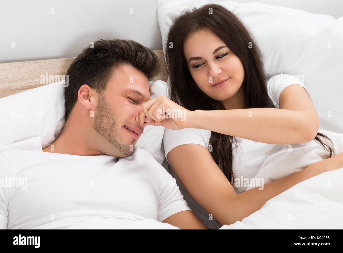 Donna Felice Tiene il marito del naso che dorme sul letto di casa Foto Stock