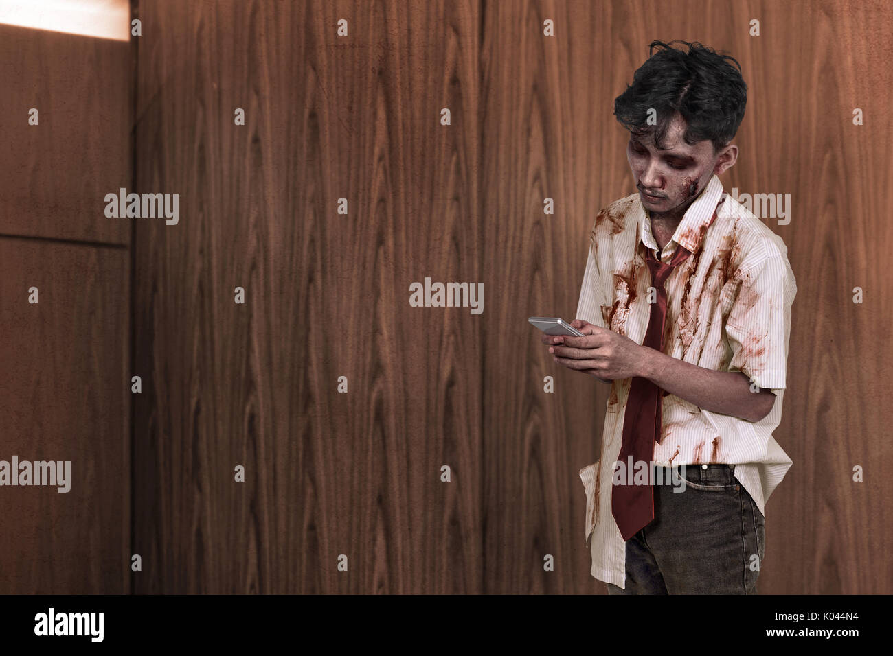 Spooky asiatici uomo zombie texting nel suo cellulare contro lo sfondo di legno Foto Stock