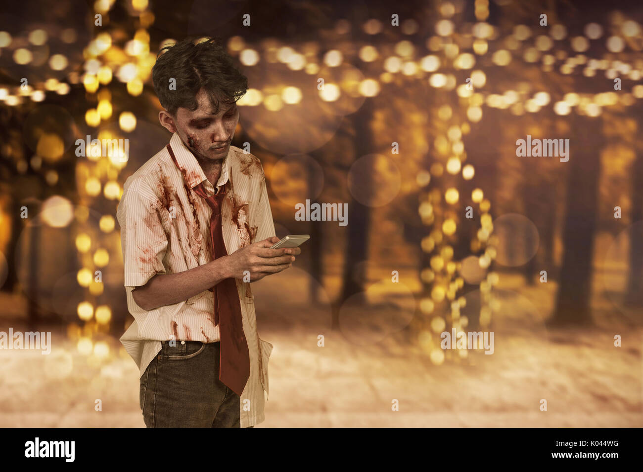 Scary asiatici uomo zombie utilizzando un mobilephone contro sfondo blured Foto Stock