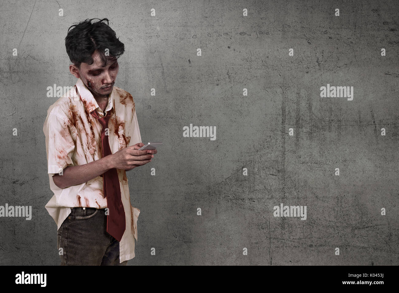 Scary asian zombie uomo azienda cellulare oltre il muro sporco sullo sfondo Foto Stock