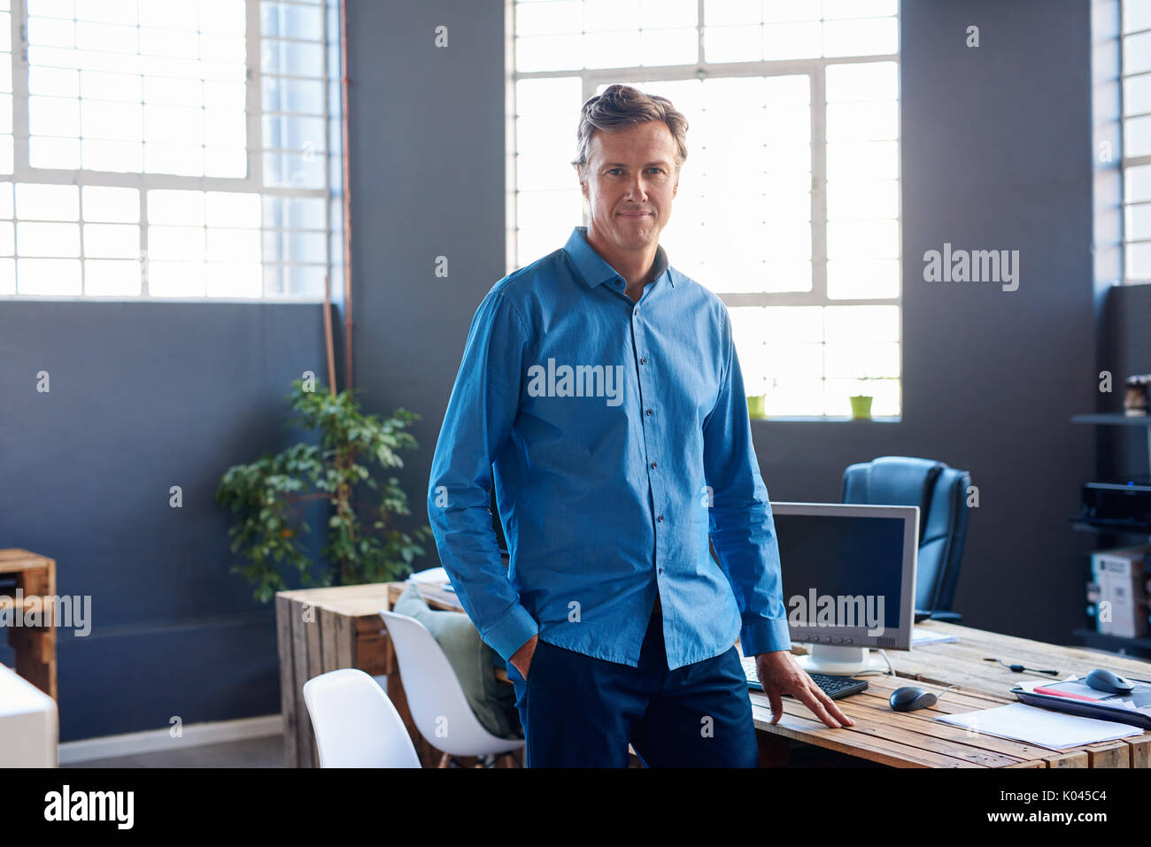 Sorridente imprenditore maturo in piedi da solo in un ufficio moderno Foto Stock