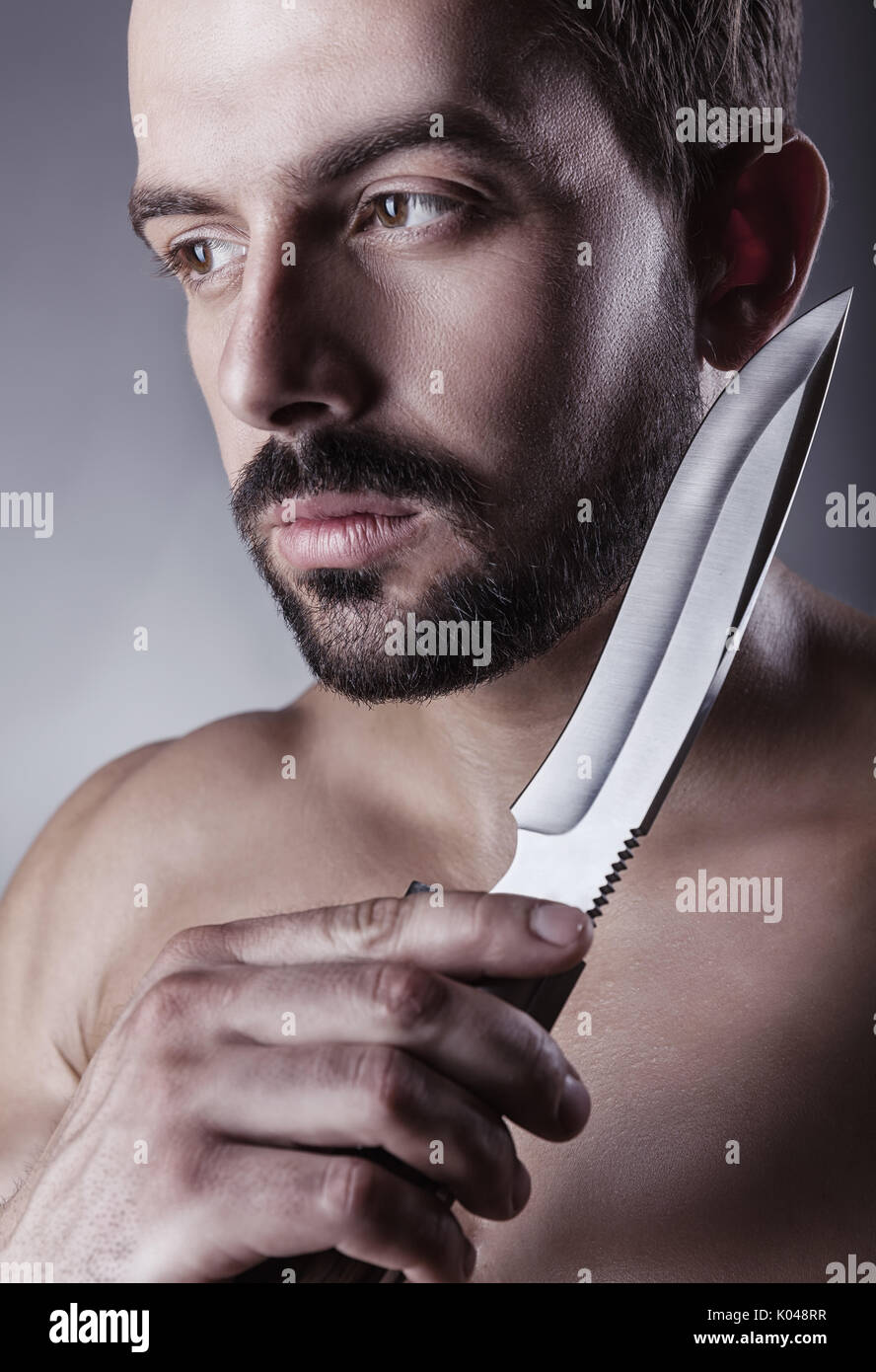 Primo piano del giovane uomo bello con la barba che mostra la lama del coltello, studio shot. Concetto di rasatura Foto Stock