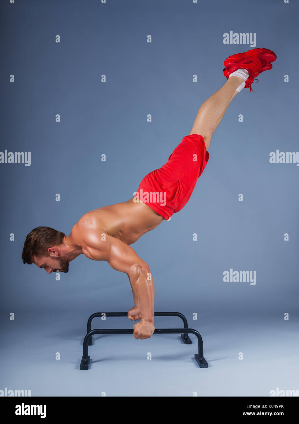 Forte atleta maschio mostra calisthenic sposta le gambe estese planche push ups sulle barre parallele, studio shot Foto Stock