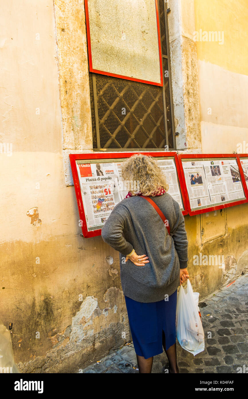 Donna che legge l'unita sul display al di fuori della locale sezione pci nel centro storico della città di Roma Foto Stock