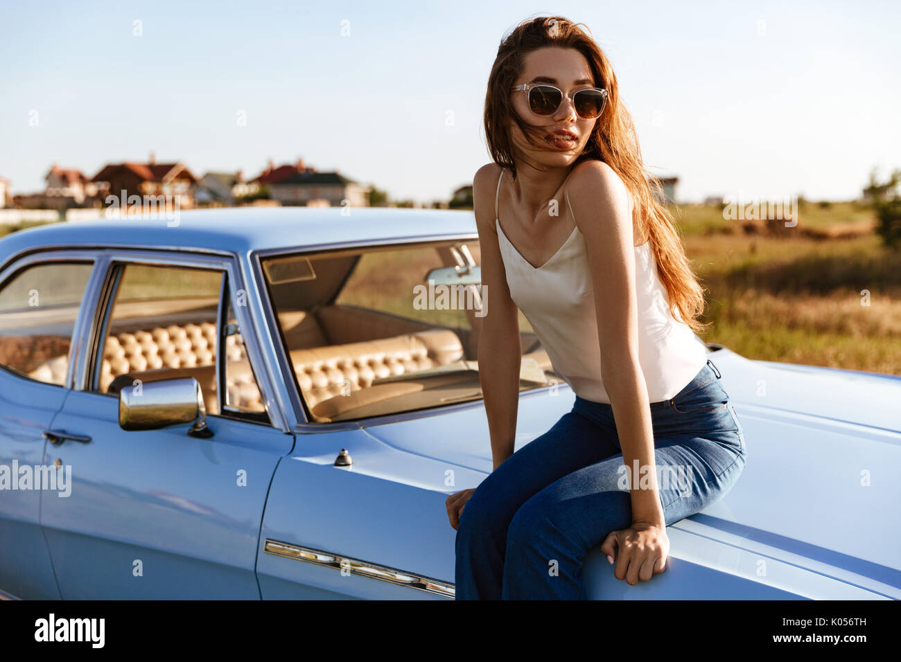 Giovane donna graziosa in occhiali da sole in appoggio mentre è seduto su un auto all'aperto Foto Stock