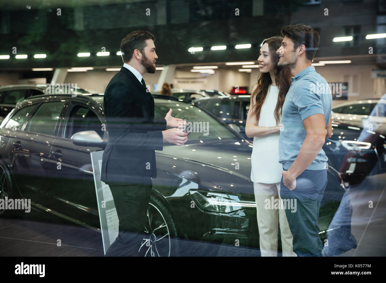 Sorridente venditore che mostra la nuova vettura di un giovane nel salone showroom Foto Stock