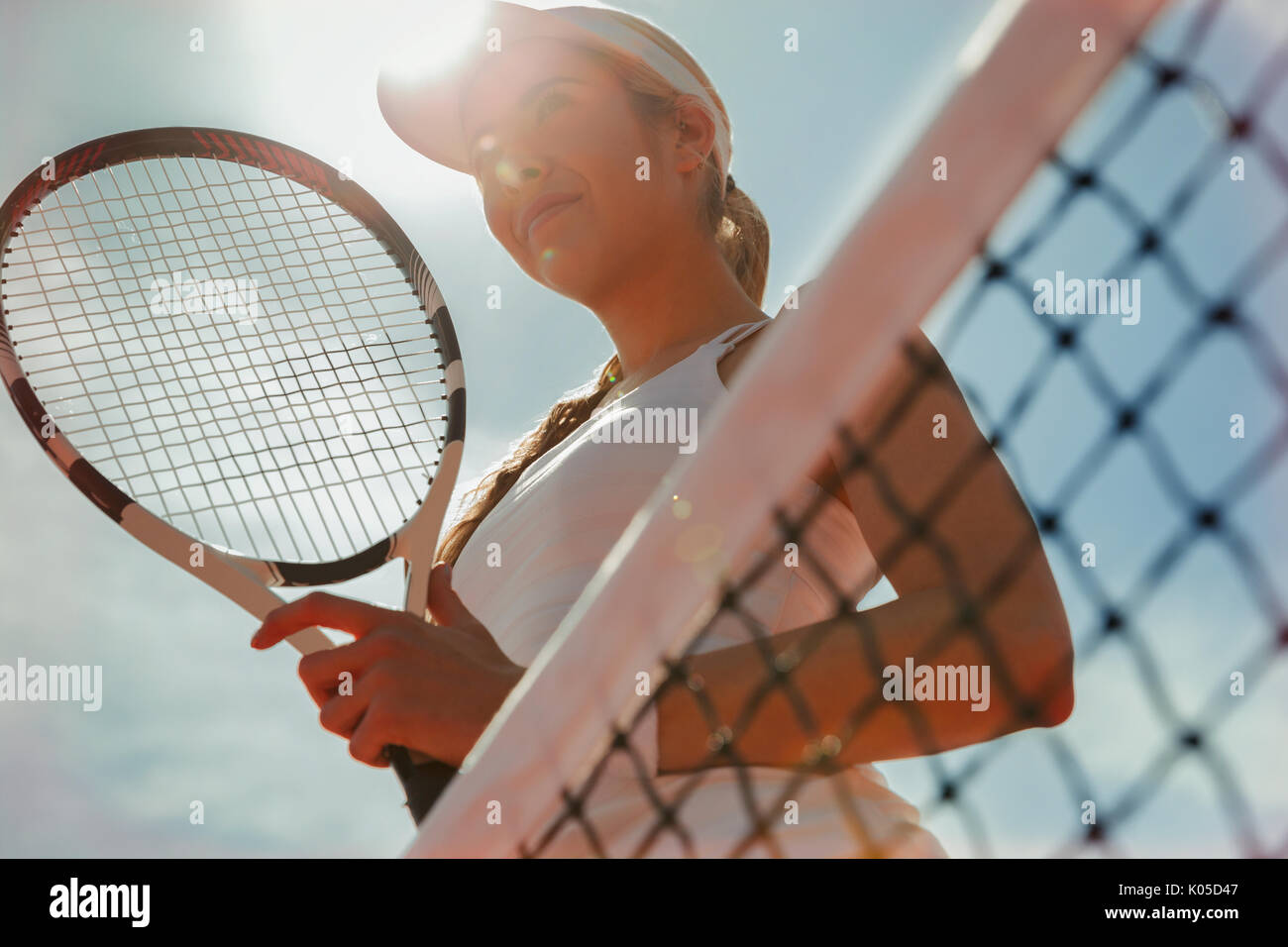 Fiducioso femmina giovane giocatore di tennis holding racchetta da tennis presso la net Foto Stock