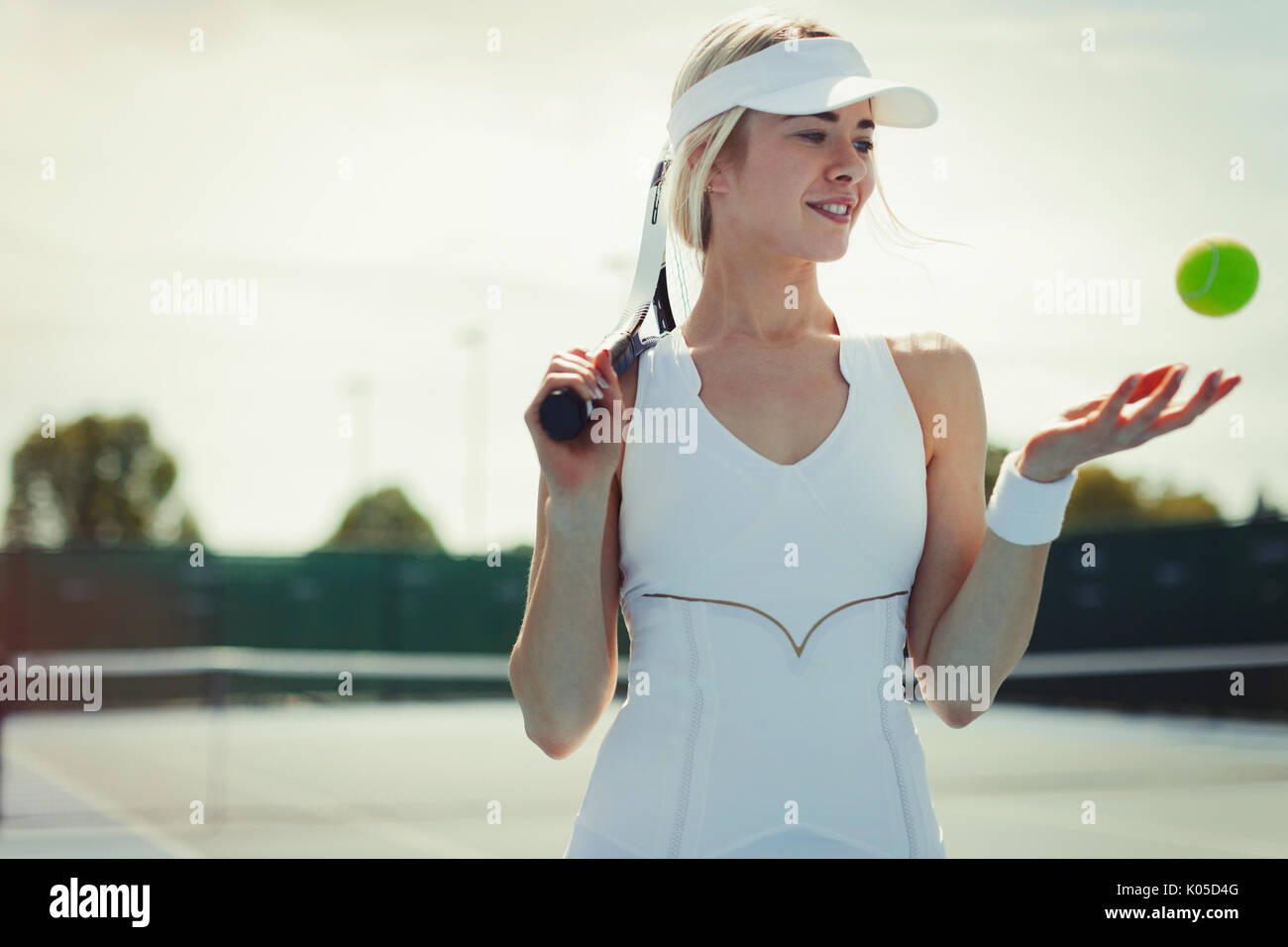 Sorridente femmina giovane giocatore di tennis holding racchetta da tennis e palla da tennis sul campo da tennis Foto Stock