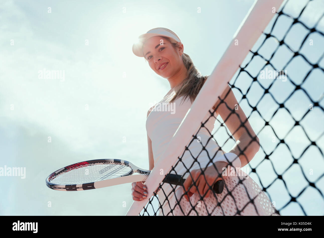 Ritratto sorridente e fiducioso di tennis femminile giocatore in possesso della racchetta da tennis presso la net sotto il cielo sereno Foto Stock