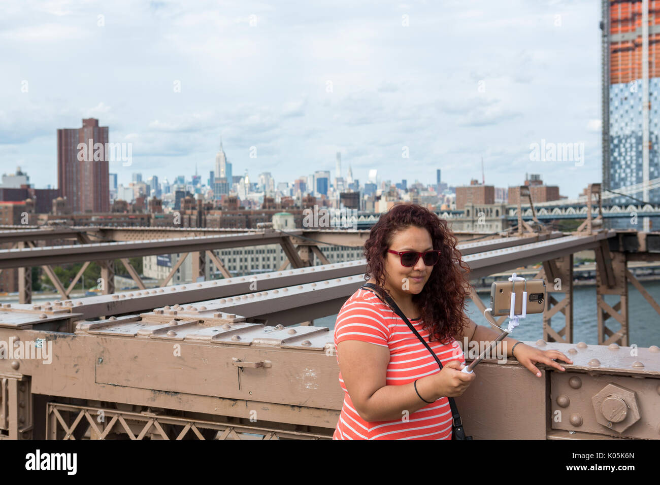 Una donna prende un selfie con un bastone sul ponte di Brooklyn a New York City, Stati Uniti d'America. Foto Stock