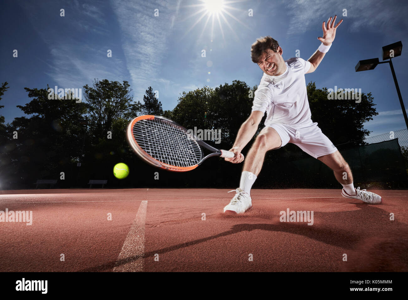 Giovane uomo giocando a tennis, raggiungendo con la racchetta da tennis su clay court Foto Stock
