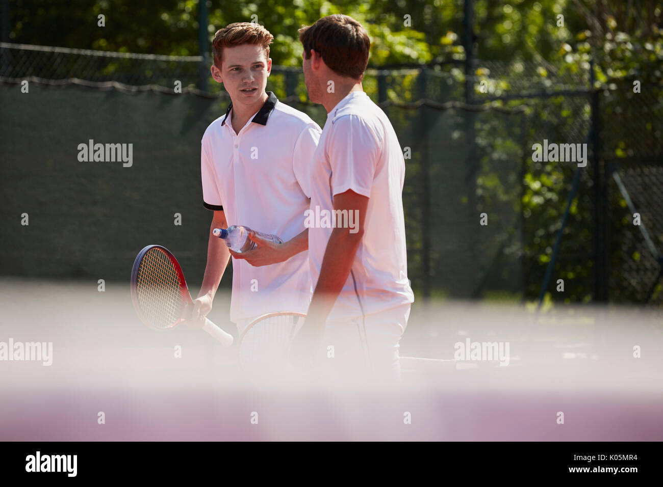 Tennis maschile i giocatori con racchette da tennis parlando sul soleggiato Campo da tennis Foto Stock