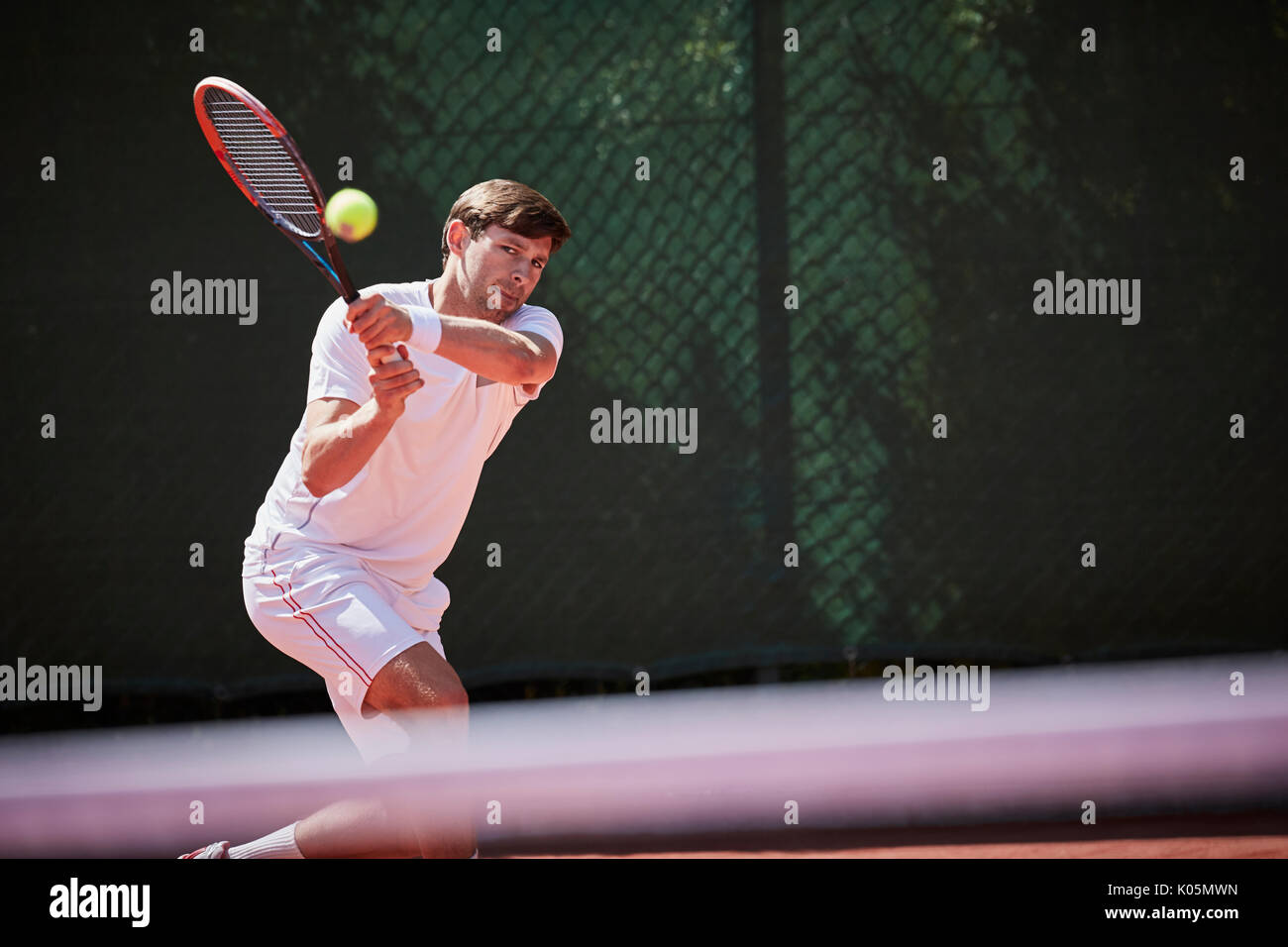 Maschio giovane giocatore di tennis giocando a tennis, colpendo la palla sul soleggiato Campo da tennis Foto Stock