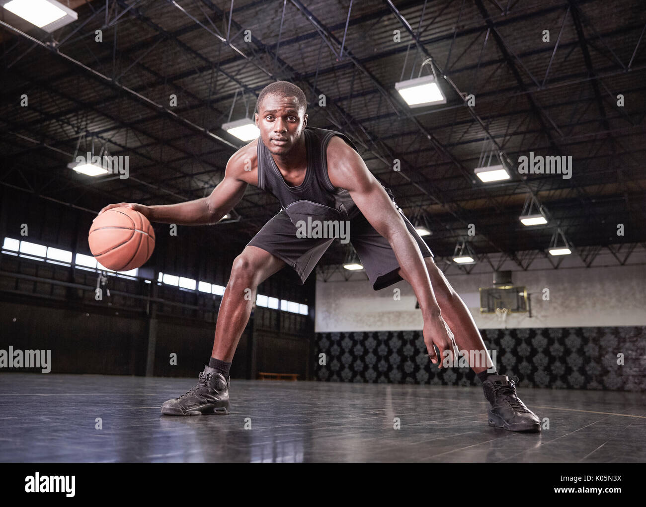 Ritratto fiducioso maschile giovane giocatore di pallacanestro di dribblare la sfera sulla corte in palestra Foto Stock