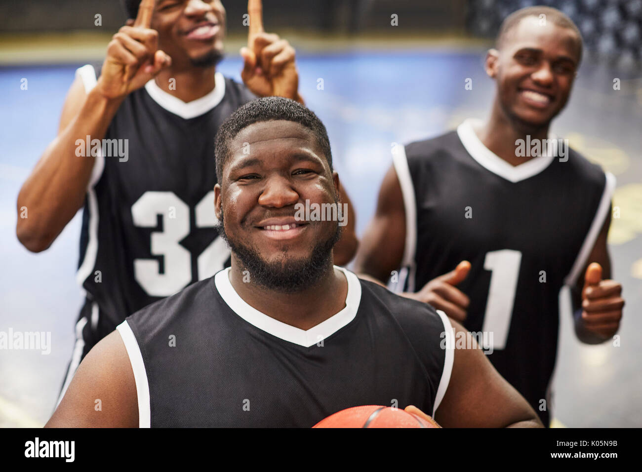 Ritratto sorridente e fiducioso maschio giovane giocatore di basket team in nero maglie gesticolando, celebrando la vittoria Foto Stock