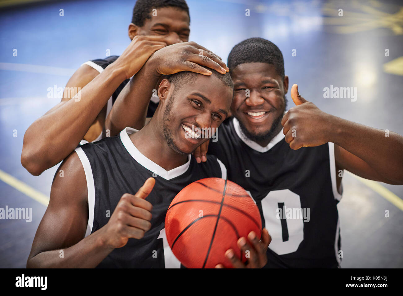 Ritratto sorridente e fiducioso maschio giovane giocatore di basket team celebrando, gesticolando pollice in su Foto Stock