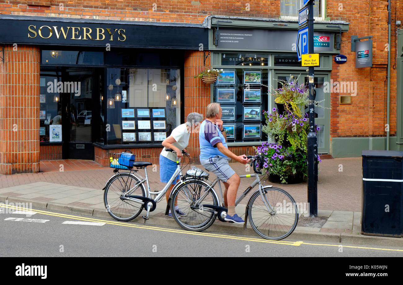 Coppia senior su biciclette cercando in agenti immobiliari windows Foto Stock