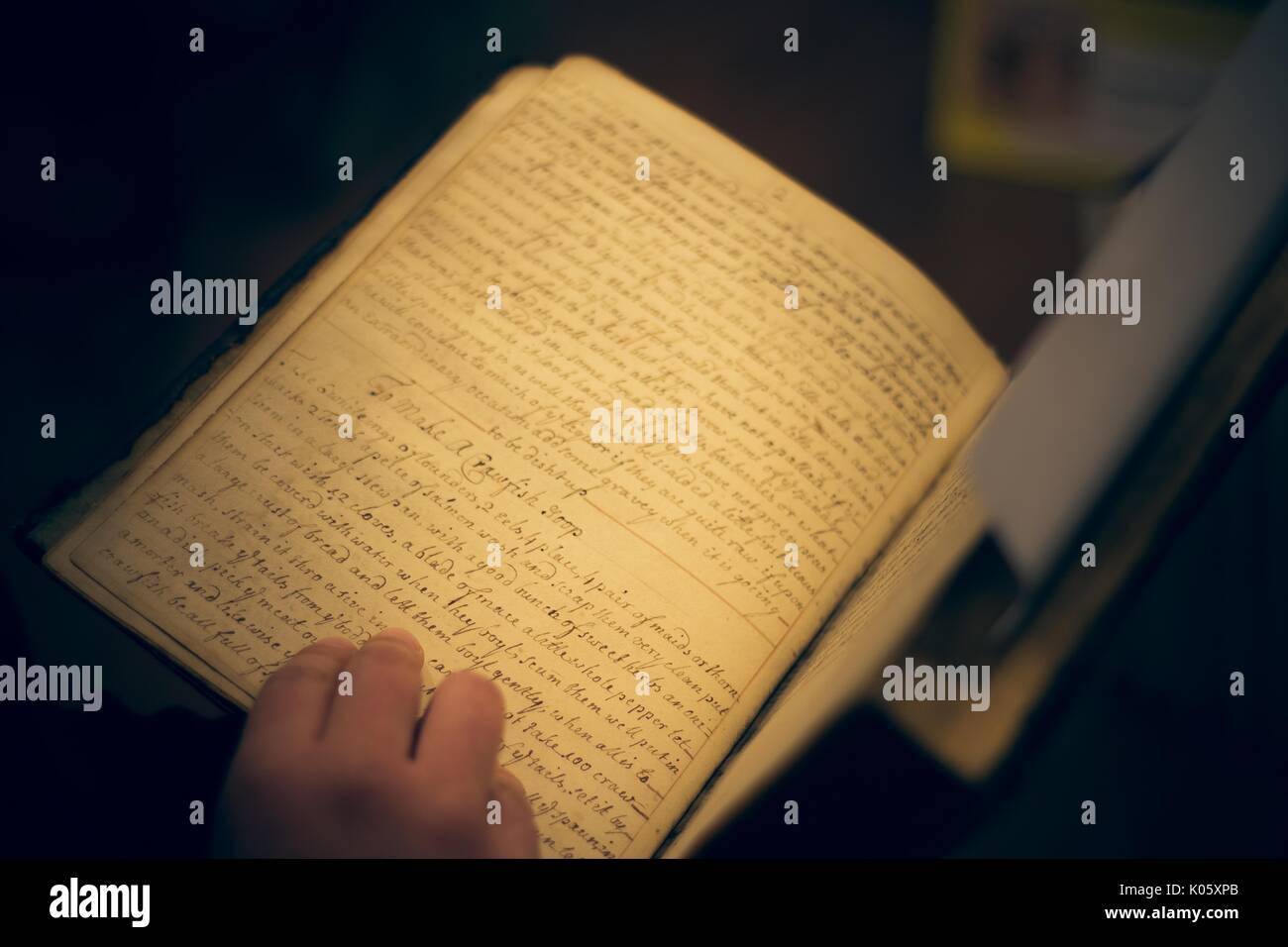 Le mani di uno studente di college mantenere aperto un antico, libri rari con intricati, corsivo script, 2016. Foto Stock