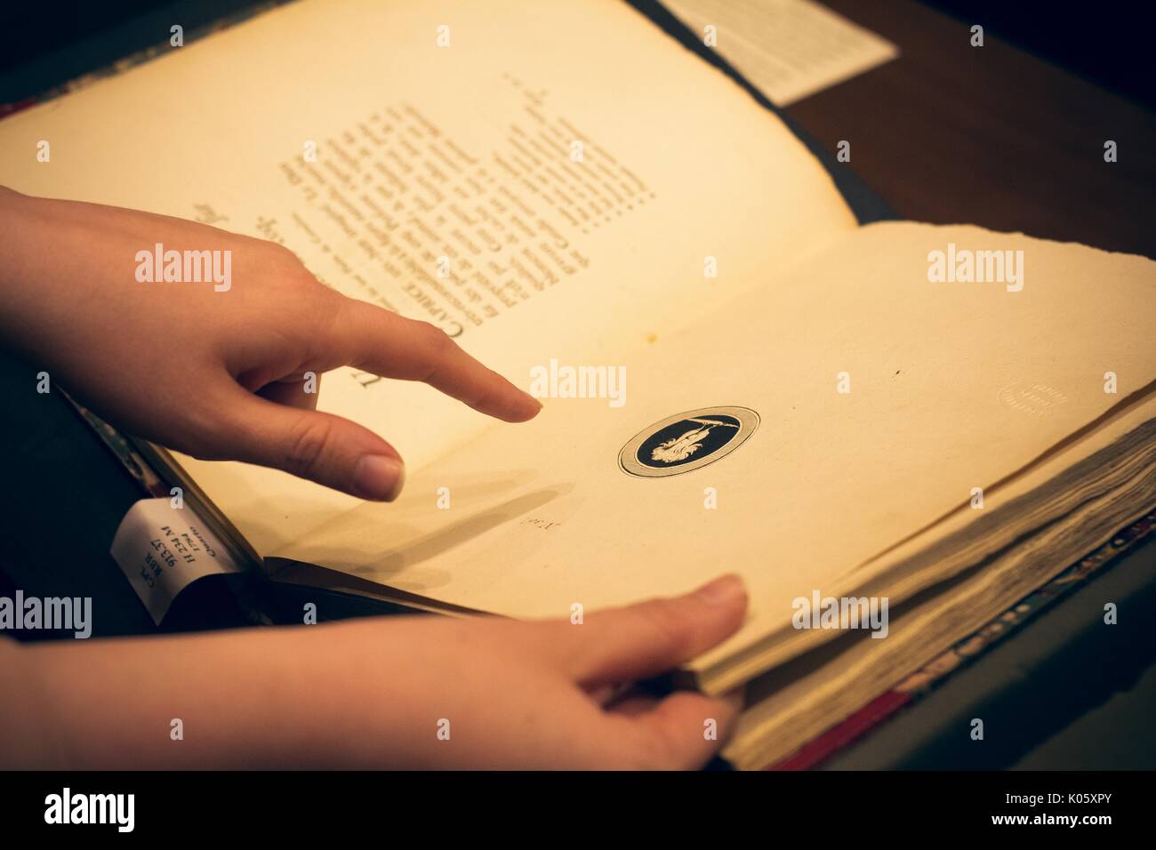 Le mani di uno studente di college azienda aprire un libro raro e puntando a un'immagine nel libro, 2016. Foto Stock