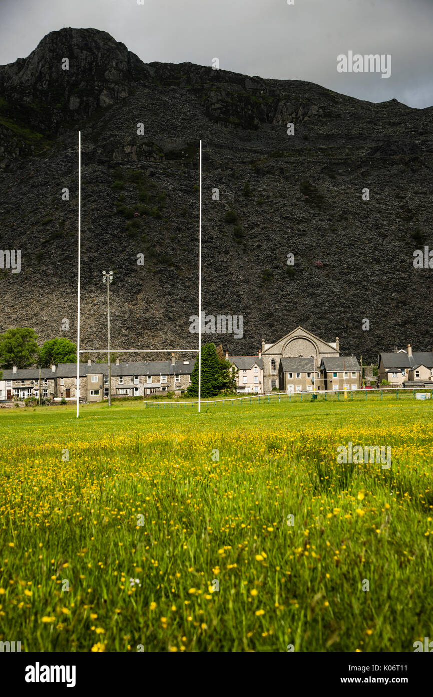 Montagne di rifiuti di ardesia che sovrasta le case, la cappella e il passo di rugby a Blaenau Ffestiniog, Gwynedd, North Wales UK Foto Stock