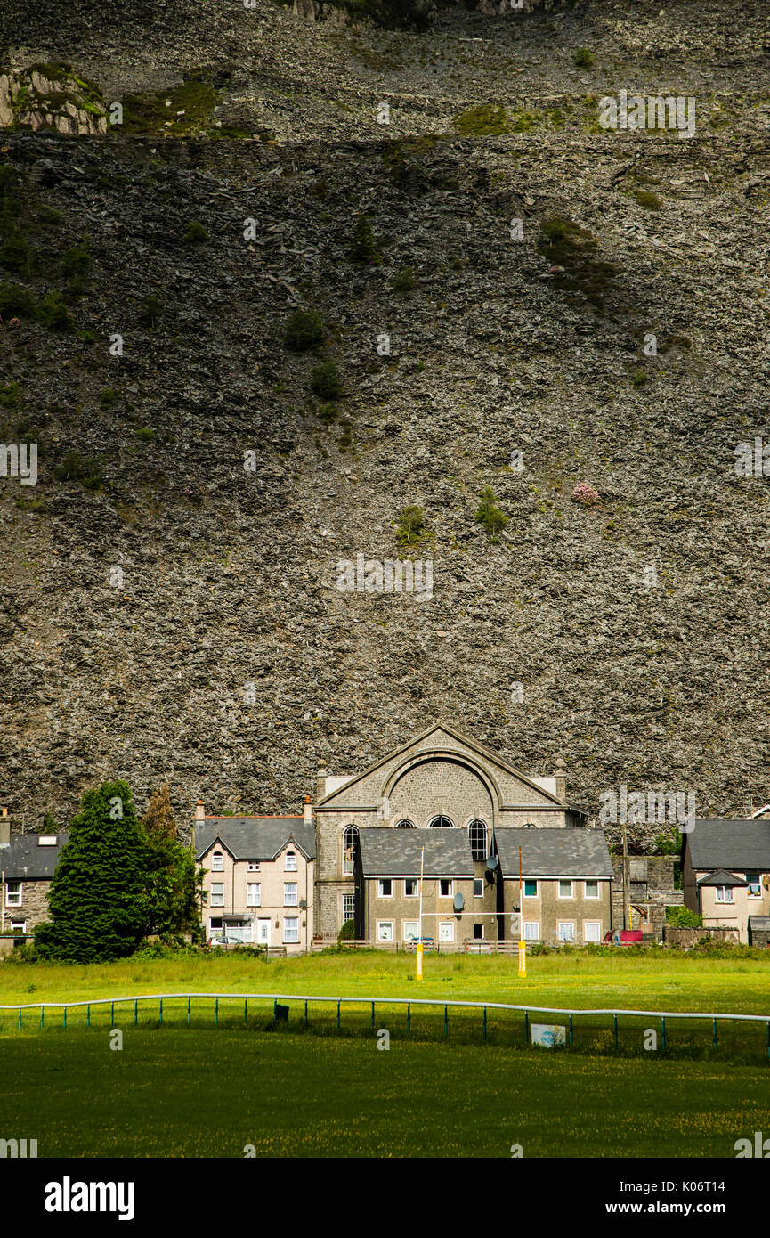 Montagne di rifiuti di ardesia che sovrasta le case, la cappella e il passo di rugby a Blaenau Ffestiniog, Gwynedd, North Wales UK Foto Stock