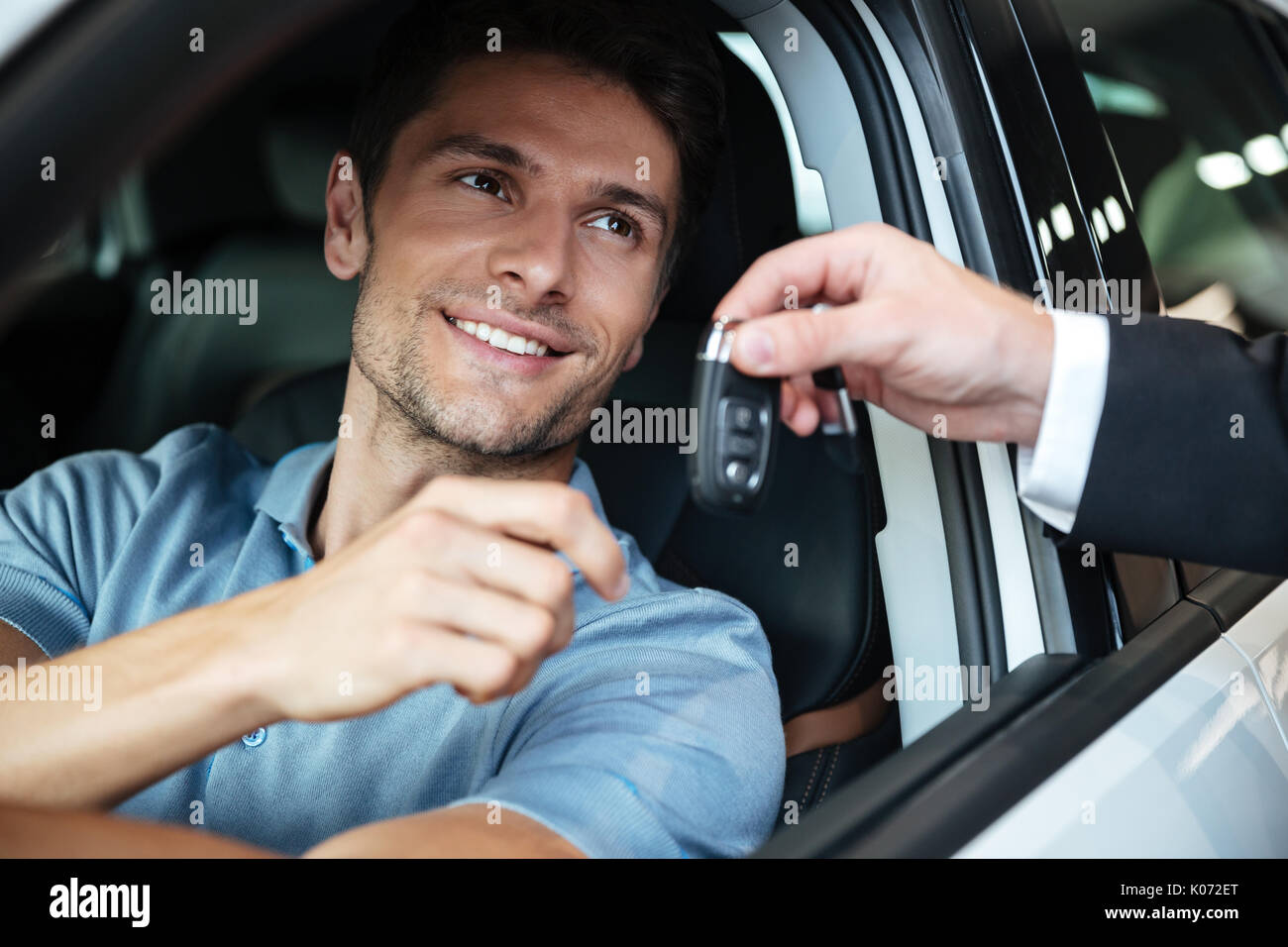 Sorridendo felice uomo seduto nella sua nuova vettura e prendere le chiavi da una mano ai concessionari presso il salone Foto Stock