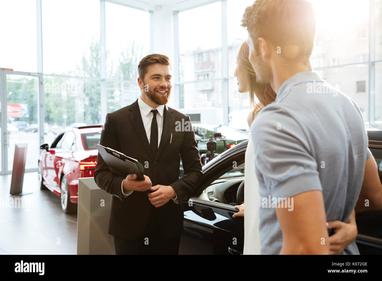 Sorridente venditore che mostra la nuova vettura di un giovane nel salone showroom Foto Stock