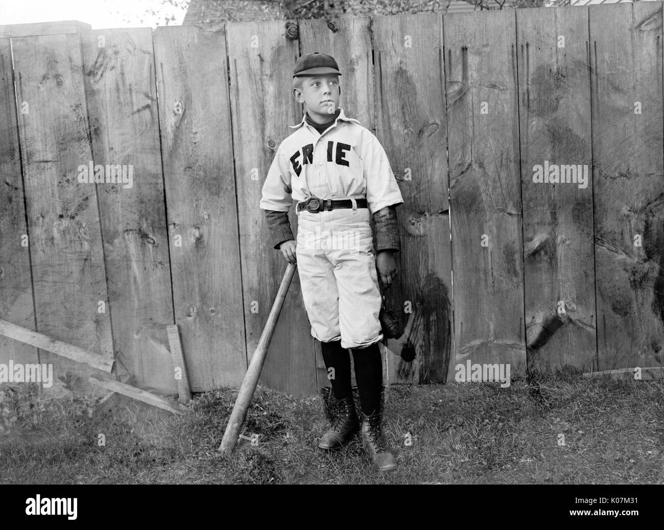 Un ragazzo in uniforme da baseball da una recinzione in America Foto Stock