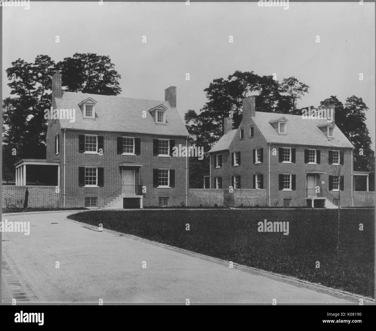 Fotografia dei due quasi identico a due piani di Roland Park Homes in Baltimore, entrambe realizzate quasi interamente in cotto, ornato di finestre e persiane, grandi alberi che si profila in background, le case accanto a un grande campo frammentarie, Stati Uniti, 1920. Questa immagine viene da una serie di documentare la costruzione e la vendita di case nel parco di Roland/Guilford quartiere di Baltimora, un tram sobborgo e una delle prime comunità prevista negli Stati Uniti. Foto Stock