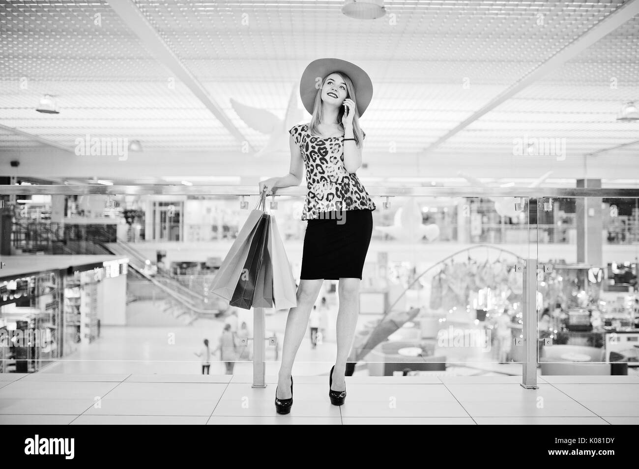 Ritratto di una donna in leopard camicetta, gonna nera a piedi nel centro commerciale per lo shopping con i sacchetti e parlare al telefono. Foto in bianco e nero. Foto Stock