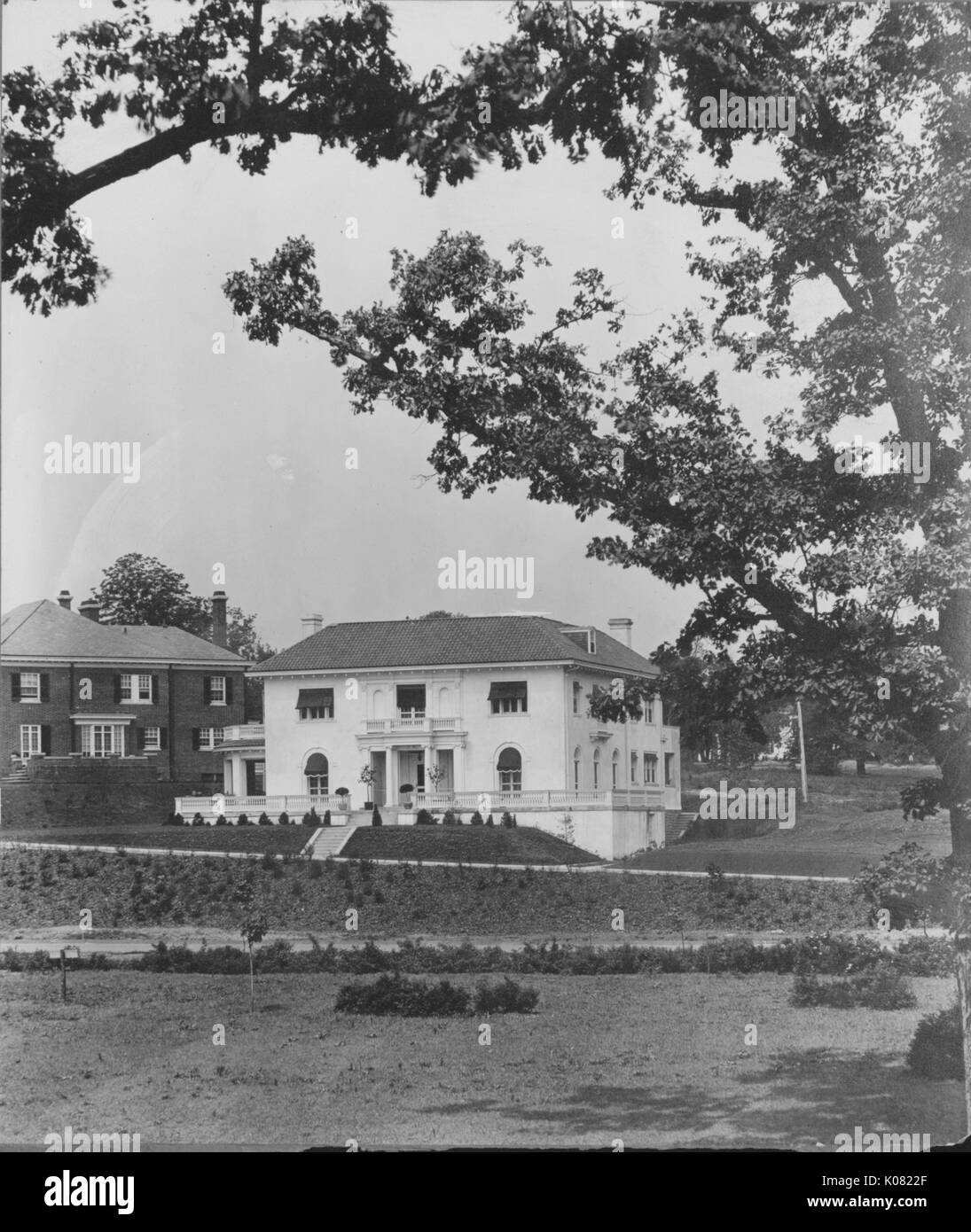 Fotografia di una Roland Park Home a Baltimora, un bianco a due piani casa su una collina erbosa con un grande portico anteriore e una facciata ornata, oltre ad una casa di mattoni di pari statura, Stati Uniti, 1920. Questa immagine viene da una serie di documentare la costruzione e la vendita di case nel parco di Roland/Guilford quartiere di Baltimora, un tram sobborgo e una delle prime comunità prevista negli Stati Uniti. Foto Stock