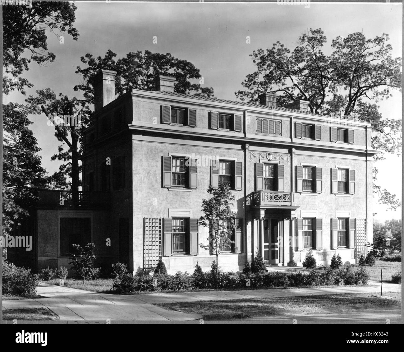 Un edificio residenziale, eventualmente un multi-fmaily home, con paesaggistici arbusti, una passerella anteriore, quattro camini, finestre con persiane e piccoli di seconda storia balcone si siede su una strada a Baltimora, Maryland, 1910. Questa immagine viene da una serie di documentare la costruzione e la vendita di case nel parco di Roland/Guilford quartiere di Baltimora, un tram sobborgo e una delle prime comunità prevista negli Stati Uniti. Foto Stock