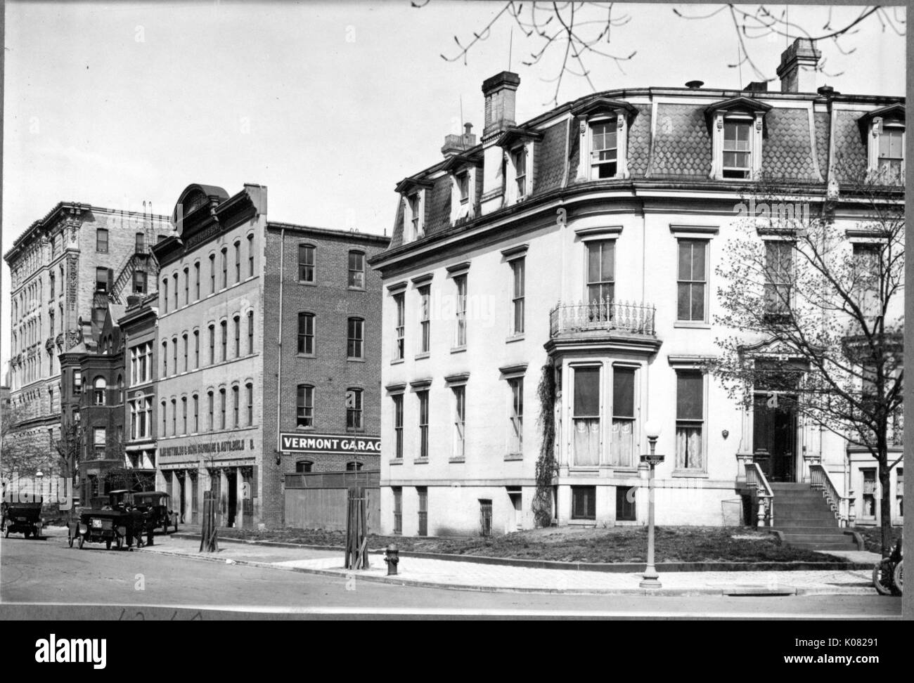 Una strada a Baltimore con un marciapiede e diversi edifici di grandi dimensioni, incluso un mattone garage parcheggio etichettato 'Vermont Garage, ' che diverse vetture stanno entrando; un grande edificio residenziale, eventualmente un appartamento edificio, con una serie di gradini che conducono alla porta anteriore, prima storia di finestre a baia, una piccola seconda storia di balcone, top story finestre dormer e vari camini; a Baltimora, Maryland, Vermont, 1910. Questa immagine viene da una serie di documentare la costruzione e la vendita di case nel parco di Roland/Guilford quartiere di Baltimora, un tram sobborgo e una delle prime comunità pianificata Foto Stock