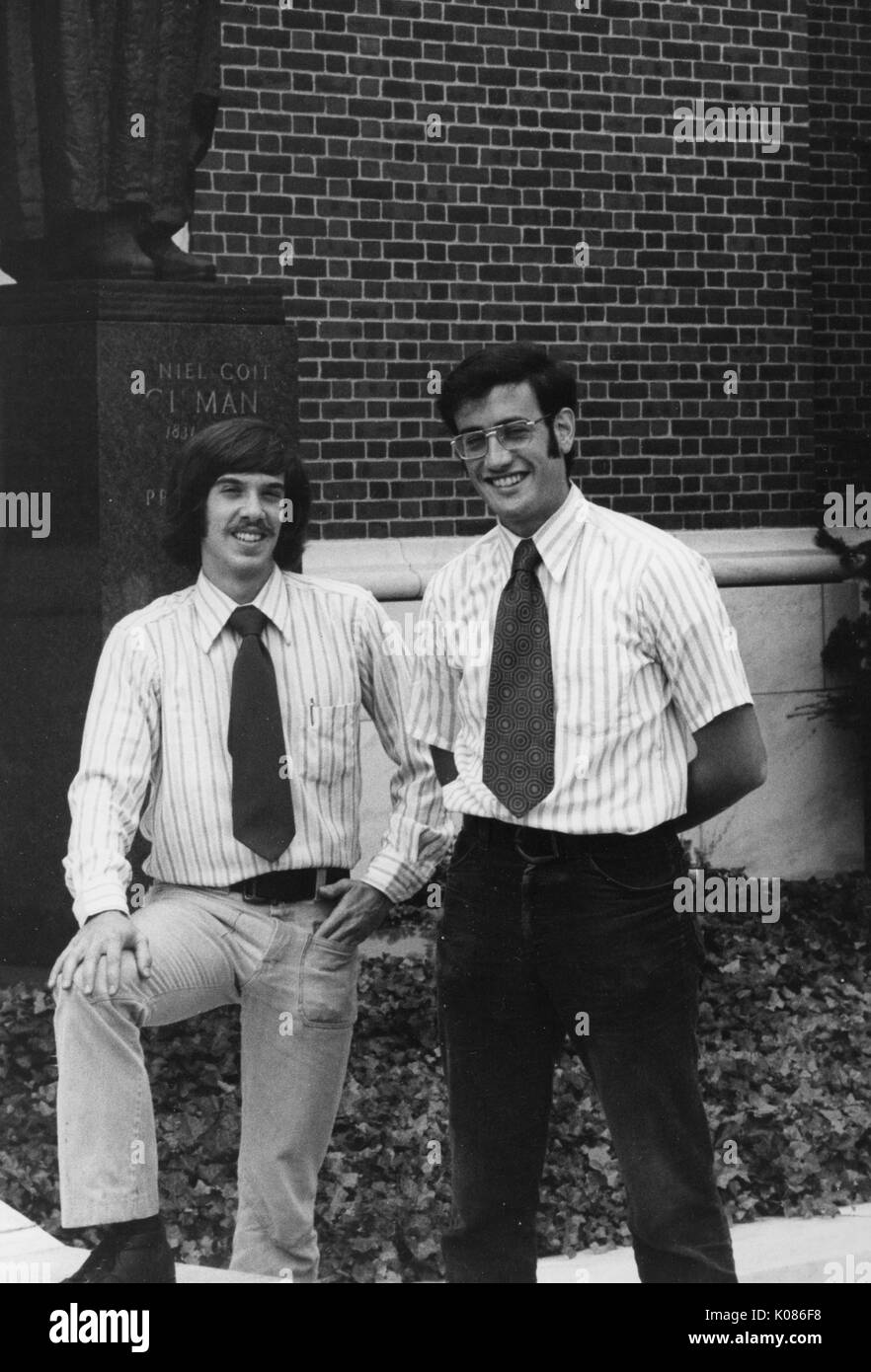 A piena lunghezza ritratto permanente di due studenti di sesso maschile della Johns Hopkins University, sorridenti e in posa di fronte alla statua di Daniel Coit Gilman, primo presidente dell'università, a fronte di un edificio in mattoni e arbusti su Homewood campus a Baltimora, Maryland, 1970. Foto Stock