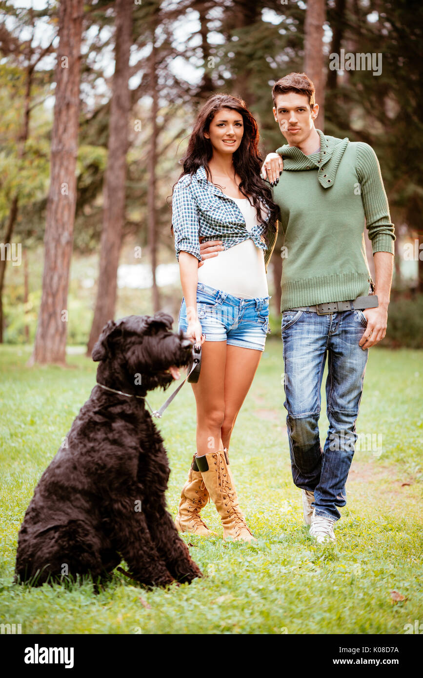 Bella coppia adorabile con un gigante nero schnauzer godendo nel parco. Foto Stock
