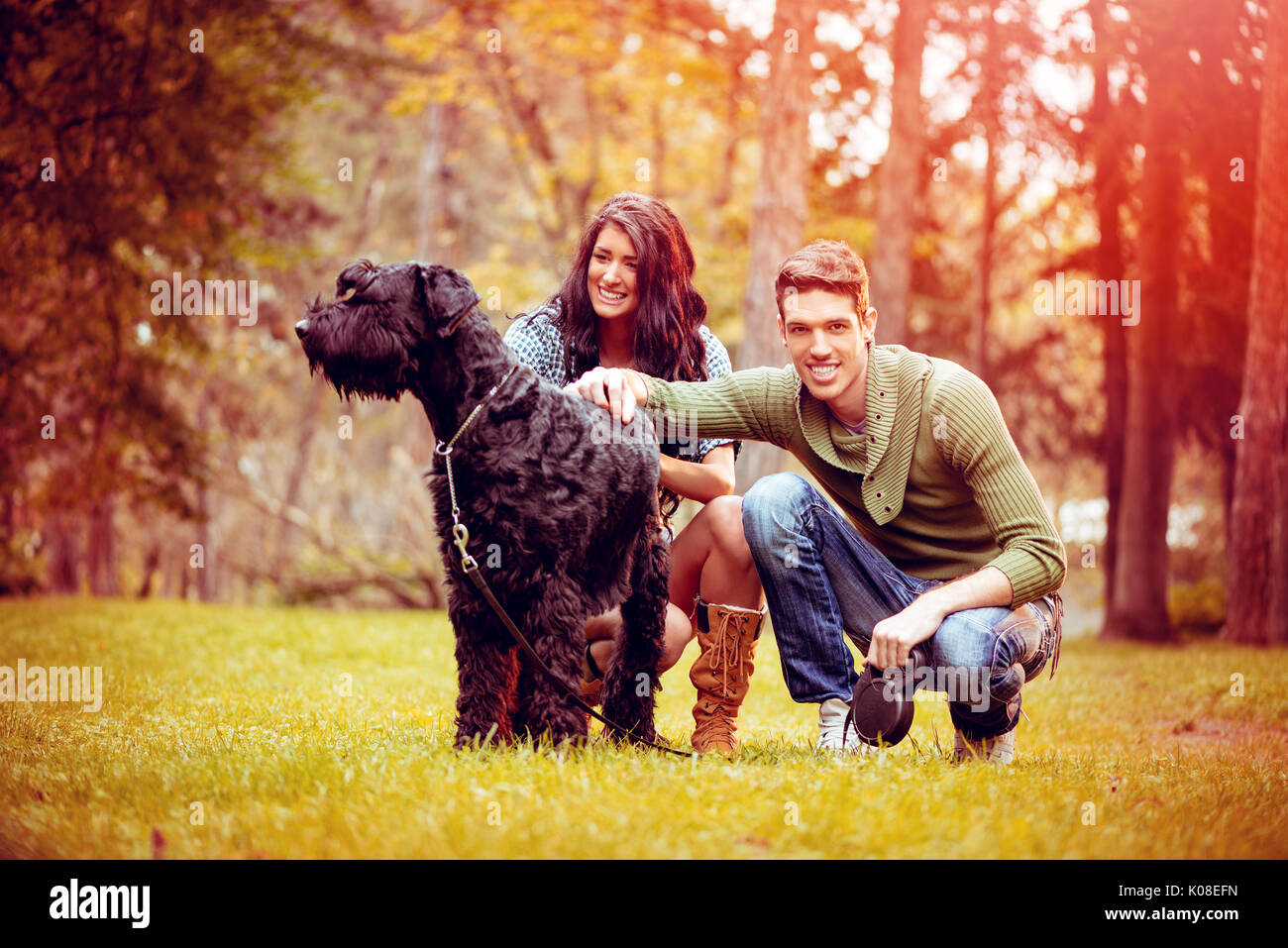 Bella coppia adorabile con un cane, un gigante nero schnauzer, godendo nel parco di colori autunnali. Foto Stock