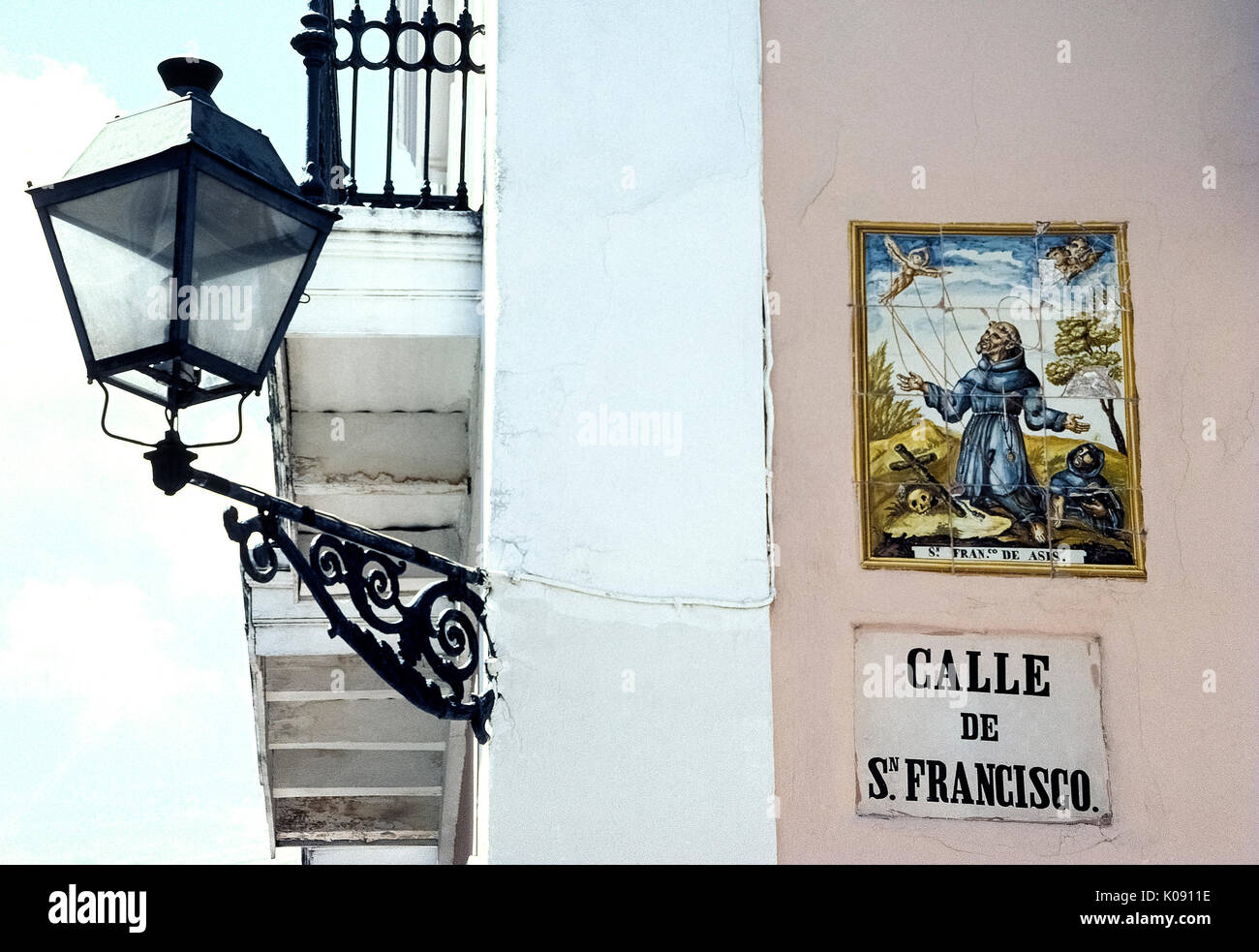 Una illustrazione di religiose di piastrelle di ceramica segna Calle de San Francisco, una strada chiamato con il nome di San Francesco di Assisi nella storica Vecchia San Juan di Porto Rico (PR), un territorio non costituite in società degli Stati Uniti nel Mar dei Caraibi. Un'annata del ferro battuto via la luce illumina il nome della strada ed illustrato e segno di notte. Foto Stock