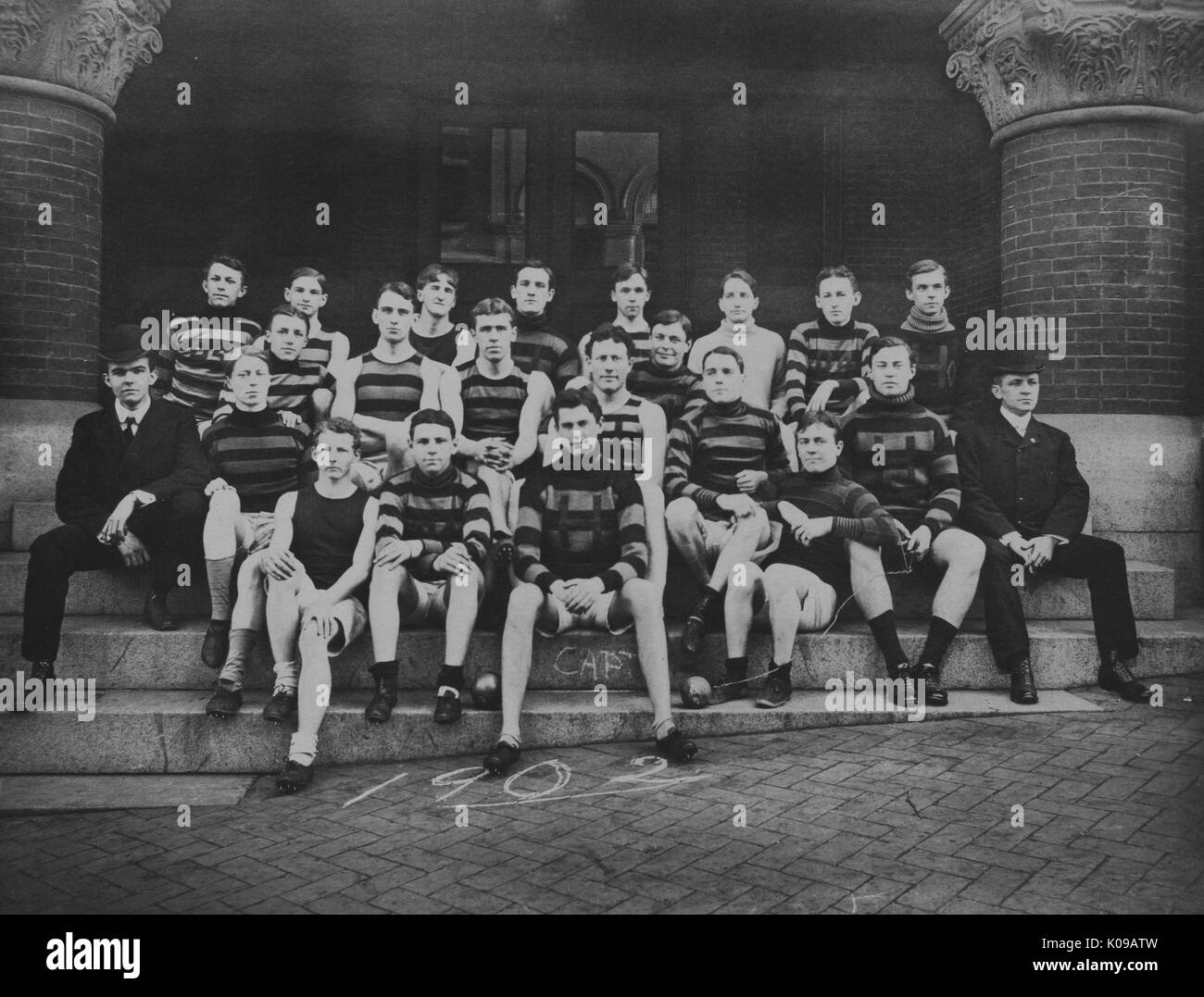 Fotografia di gruppo, la via e il team del settore è insediato in un ritratto formale sui gradini nel loro team di uniformi, '1902' scritto in gesso sulla terra davanti, 1902. Foto Stock