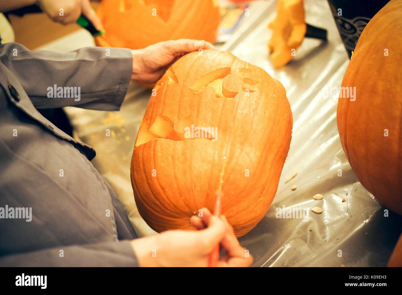 Le mani di uno studente mostrato carving una faccia in una zucca con un coltello sottile, altri che circondano le zucche di Halloween presso la Johns Hopkins University di George Peabody Library, Ottobre 31, 2015. La cortesia Eric Chen. Foto Stock