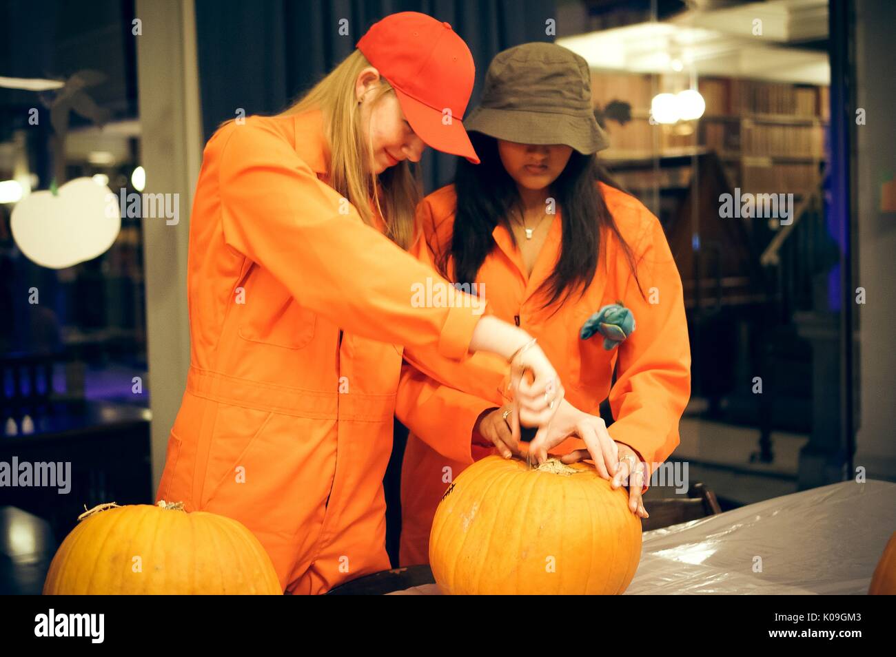 Due studenti del college lavorano insieme a intagliare lo stelo di una zucca, essi sono vestiti in tute arancioni come caratteri dal racconto di "buchi", Halloween presso la Johns Hopkins University di George Peabody Library, 2015. La cortesia Eric Chen. Foto Stock