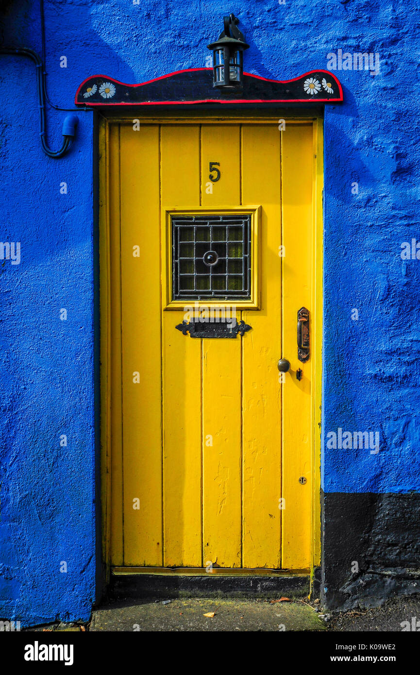 Una luminosa gialla porta si staglia contro il blu esterno di un piccolo cottage Foto Stock