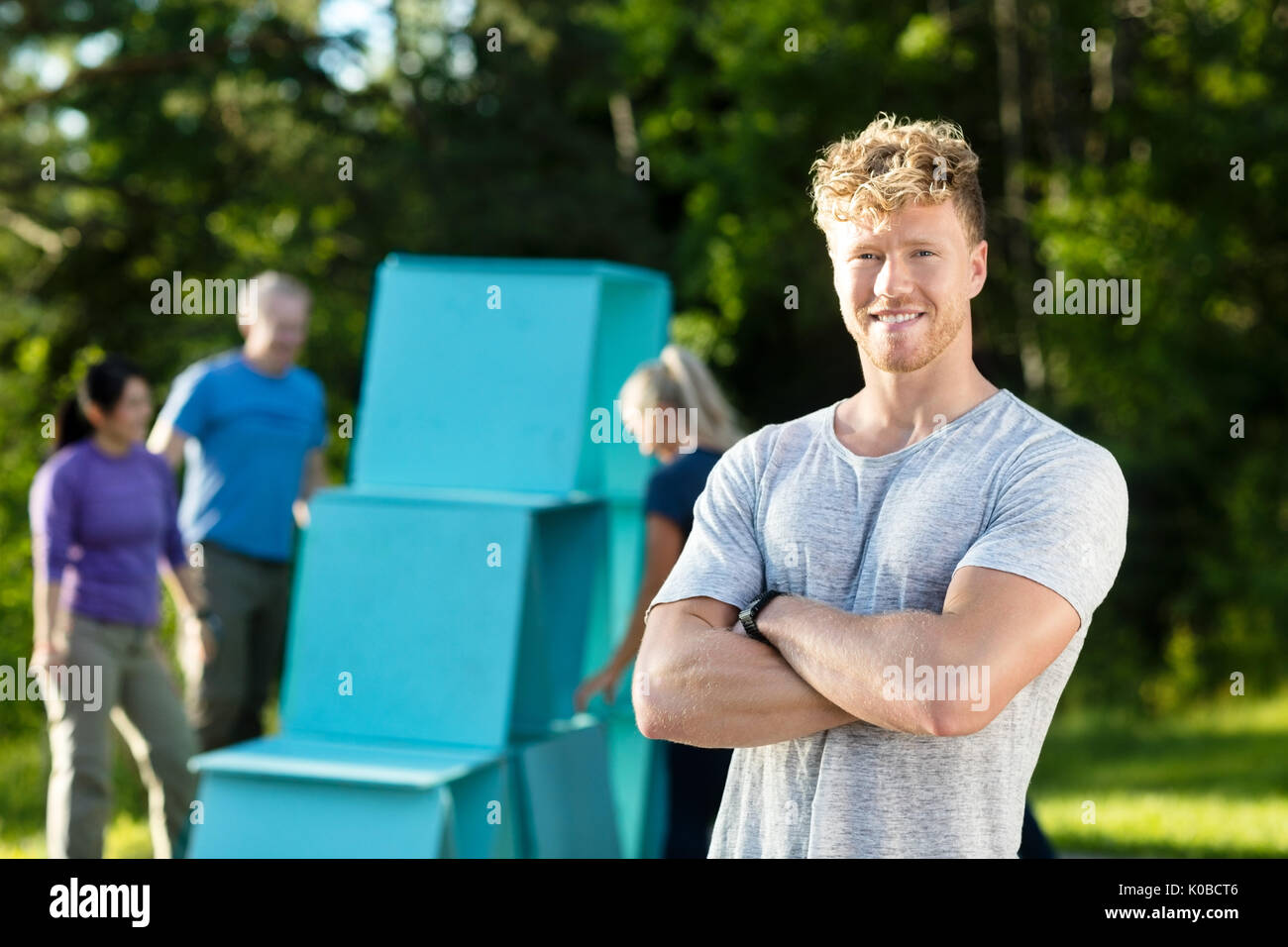 Sorridente giovane uomo in piedi con le braccia incrociate mentre gli amici facendo Pyr Foto Stock