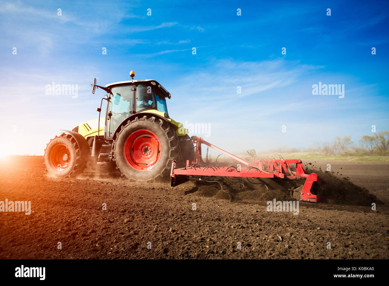 Il trattore lavora su terreni agricoli sul tramonto Foto Stock